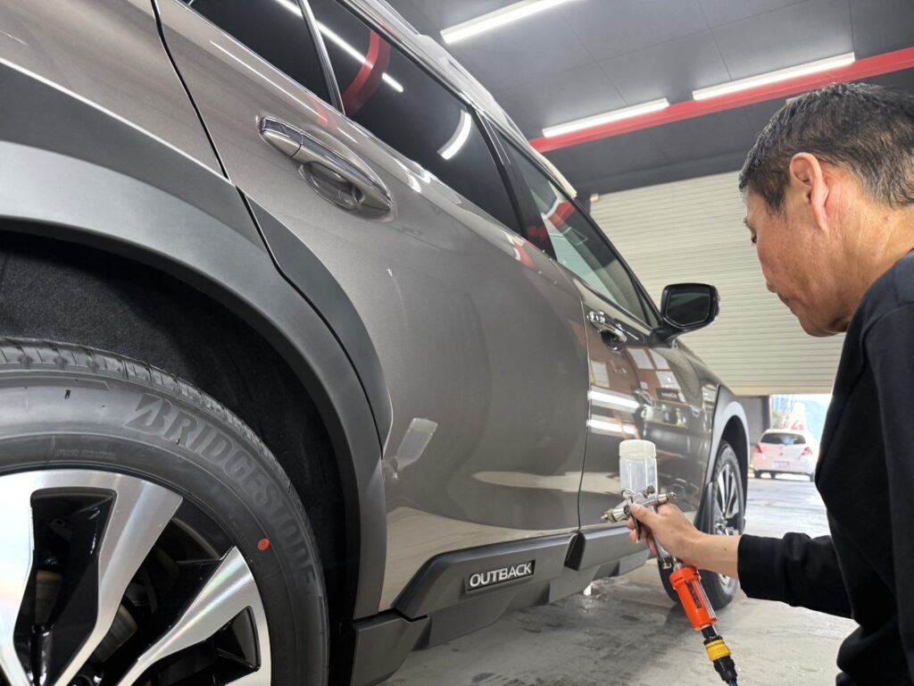 スプレーガンで樹脂部分にコーティング剤を吹きかけている様子。