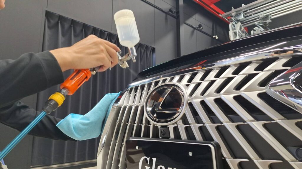 レクサスのグリル部分にスプレーガンでコーティング剤を吹きかけている様子