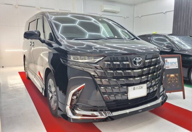 Front view of a glossy black Toyota minivan on a red carpet in a bright showroom.