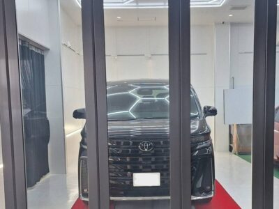 Front view of a black Toyota SUV inside a bright showroom, seen through glass doors with a red carpet under the car.