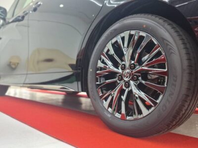 Close-up of a glossy chrome alloy wheel on a dark car, Dunlop tire, on a red showroom carpet.