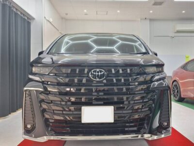Front view of a glossy black Toyota SUV in a showroom, headlights on, chrome grille and license plate area visible on a red carpet.