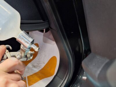 Person holding a spray gun near the car's door frame, likely preparing to apply paint or sealant inside the vehicle
