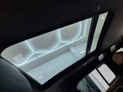 Inside a car, view through the panoramic sunroof at a white ceiling with glowing geometric LED lines outside.