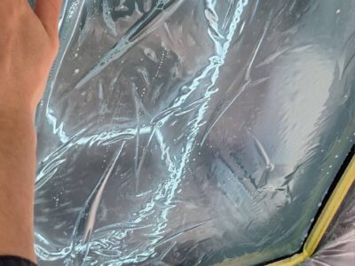 Close-up of a hand resting on a glass window covered with clear protective film and yellow tape along the bottom edge.