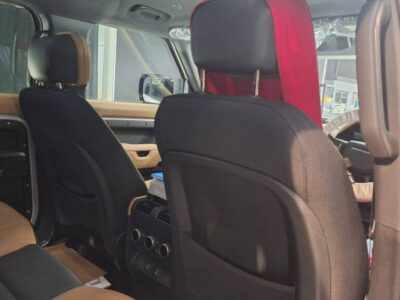 Interior of a car viewed from the back seat, tan and black upholstery with rear passengers' seats visible and a red headrest cover in the front.