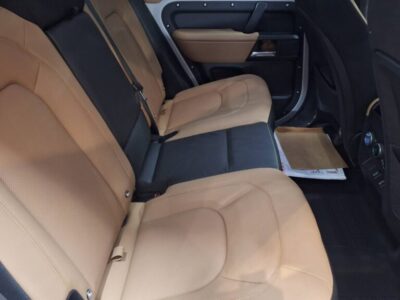 Back seat of a car with tan leather seats and a black center section, door panel visible on the side.
