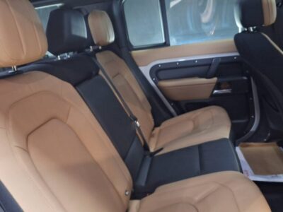 Inside a car rear cabin with tan leather seats and black center seat, beige door panels, and headrests visible