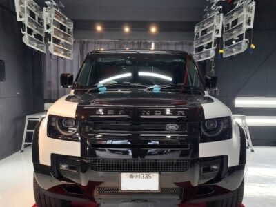 Front view of a two-tone (black and white) Land Rover SUV in a studio setting with stage lighting above and red carpet beneath the vehicle.