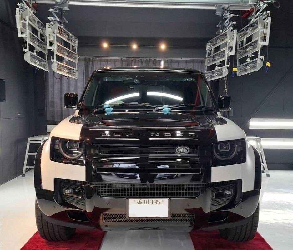 Front view of a two-tone (black and white) Land Rover SUV in a studio setting with stage lighting above and red carpet beneath the vehicle.