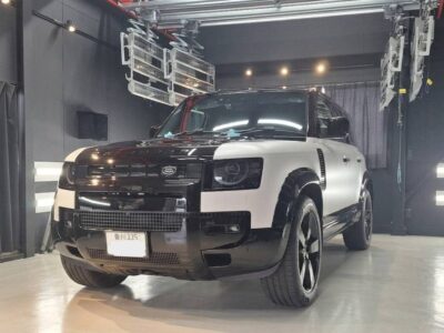 Two-tone black and white Range Rover SUV parked in a studio with industrial lighting and equipment overhead, front-left view.