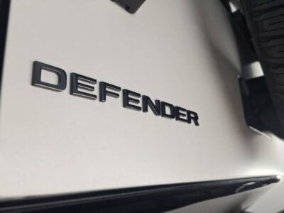 Close-up of a car side panel with the DEFENDER badge and a tire in the background.