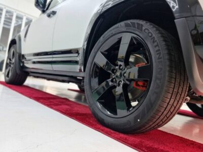 Low-angle close-up of a black alloy wheel with red brake calipers on a white car on a red showroom carpet.
