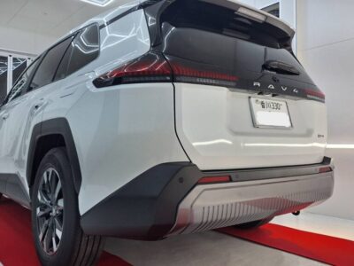 Rear view of a white Toyota RAV4 SUV in a bright dealership showroom on a red carpet, taillights lit.
