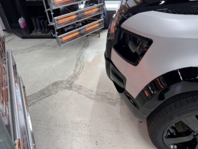 White and black SUV parked in a garage, with orange heat lamps and equipment visible in the background.