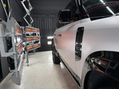 White luxury car in a controlled test lab with infrared heater panels to the left.