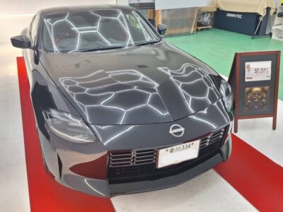 Gray Nissan sports car on a red carpet in a showroom, with distinctive hexagonal light reflections on the windshield and hood.