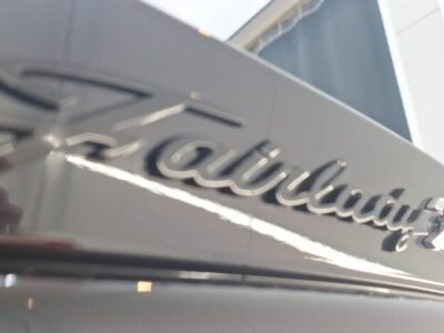 Close-up of a glossy car badge with cursive lettering on a dark surface, reflecting light.