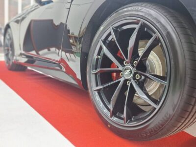 Close-up of a black alloy wheel with a red brake caliper on a sleek car, parked on a red carpet in showroom lighting.