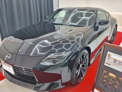 Front three-quarter view of a dark gray Nissan sports car on a red showroom carpet, with a display board beside it.