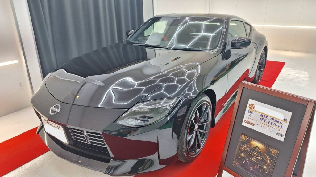 Front-left view of a sleek gray Nissan sports coupe on a red showroom carpet, in a bright showroom setting in front of a display board.