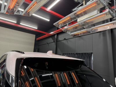 White SUV inside a modern garage with orange infrared heaters above and a gray wall backdrop nearby