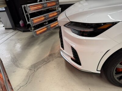 White car front end visible in a garage with orange infrared heater panels in the background