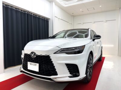 Front view of a white Lexus SUV on a red showroom carpet, indoors with bright lighting and black grille accents.