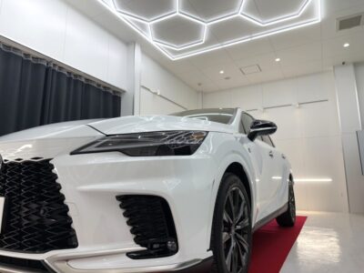 White luxury SUV on a red showroom carpet, photographed from a low angle with geometric ceiling lights above.