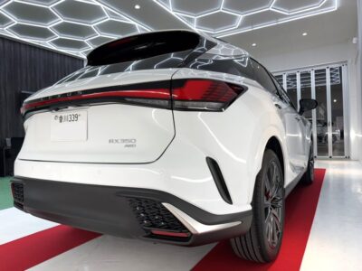 White Lexus RX350 AWD SUV shown from the rear three-quarter in a glossy showroom with hexagonal ceiling lights reflected above it on bright flooring.