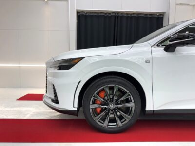 White luxury SUV front wheel, orange brake calipers, and bold alloy wheel in a showroom with red carpeted floor.