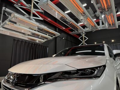 White car in a showroom or studio with overhead lighting and equipment above it, close-up of the front end and headlights