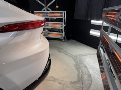 White car rear quarter panel in a garage-like space with orange infrared heaters nearby