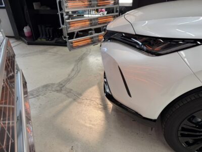Front-right view of a white car in a workshop, showing the headlight and sleek bumper.