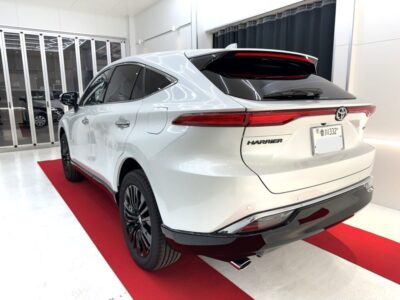 Rear three-quarter view of a white Toyota Harrier SUV in a bright showroom on a red carpet.