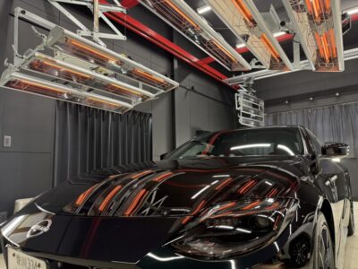 Black Nissan sports car in a climate/testing chamber with overhead infrared heaters overhead and reflections on the car body.