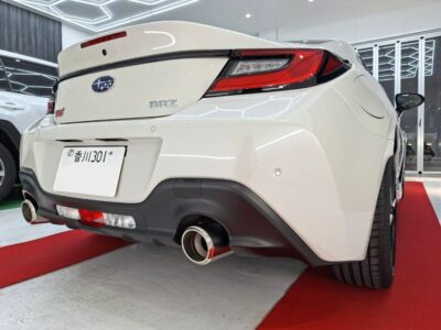 Rear view of a white Subaru BRZ in a showroom on a red carpet, highlighting the dual exhausts and taillights.