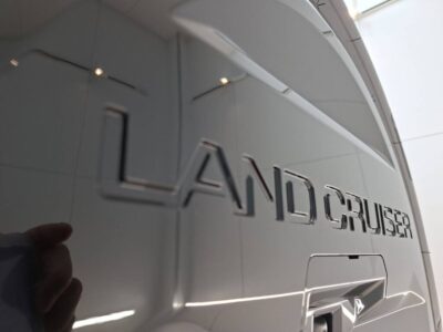 Rear of a white Toyota Land Cruiser with chrome badge reading 'LAND CRUISER' on the tailgate