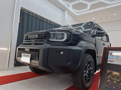 Black Toyota SUV on a red-carpet showroom floor with bright geometric ceiling lights, showcased indoors. Interpretive caption: vehicle display.