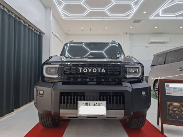 Front view of a black Toyota SUV on a red display mat in a bright showroom with hexagonal LED ceiling lights