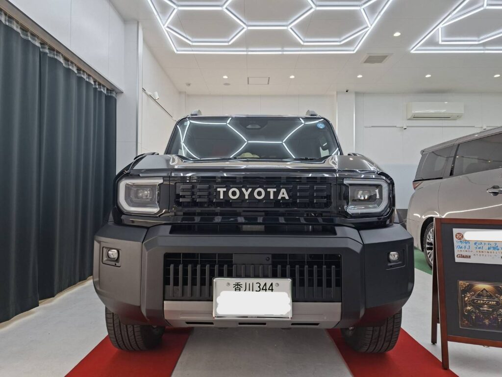 Front view of a black Toyota SUV on a red display mat in a bright showroom with hexagonal LED ceiling lights