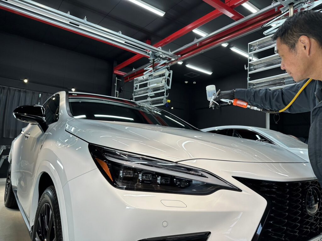Technician spraying coating onto a white car with a pneumatic tool in a workshop