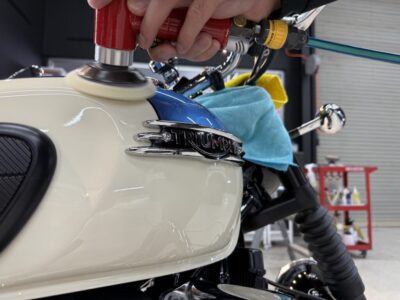Mechanic polishing a Triumph motorcycle fuel tank with a red electric polisher.