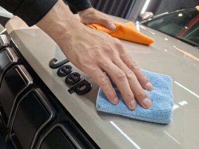 Person cleaning the hood of a Jeep with a blue microfiber cloth.