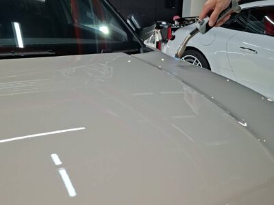 Technician uses a handheld testing device on the hood of a white Jeep inside a showroom or workshop.