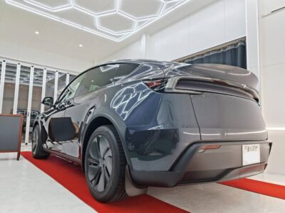 Rear three-quarter view of a gray electric SUV on a red carpet inside a bright showroom.