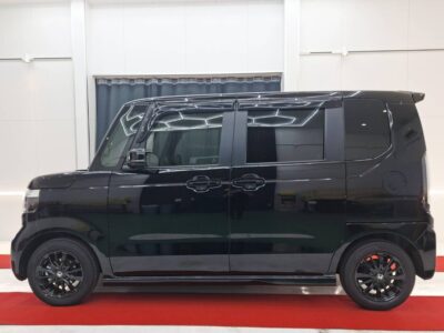 Black compact van in a showroom, side profile view with tinted windows and black alloy wheels on a red carpeted floor