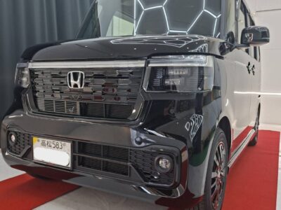 Front-angle view of a glossy black Honda van on a red carpet in a showroom, showing the chrome grille and LED headlights.