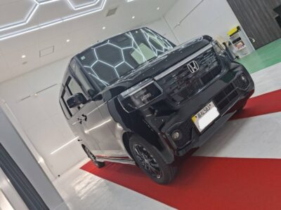 Black Honda minivan displayed indoors on a red carpet, shown from the front‑quarter with bright showroom lighting and white walls.