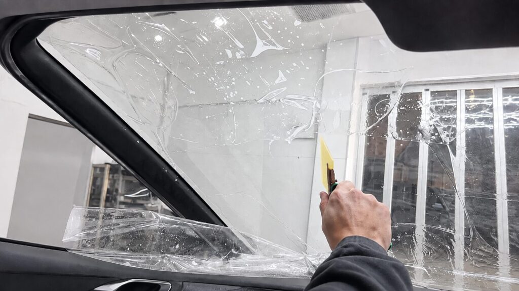 テスラ車種を含めた豊富な施工実績 - 香川でガラスコーティング専門店ならカーケアグランツ|四国の施工実績多数 フロントガラスにフィルムを貼っている様子
